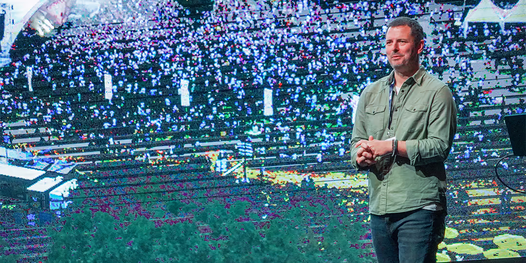 Talare på scen framför en stor, pixlig LED-skärm med publik i bakgrunden.