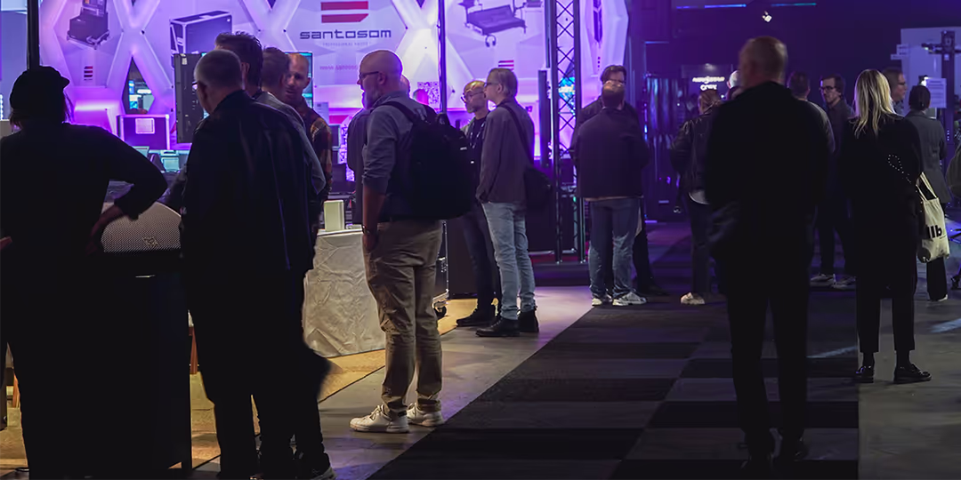 LLB Expo Varför ställa ut Besökare i en mörk mässhall står och pratar vid utställarmontrar; lila belysning lyser upp gångarna.