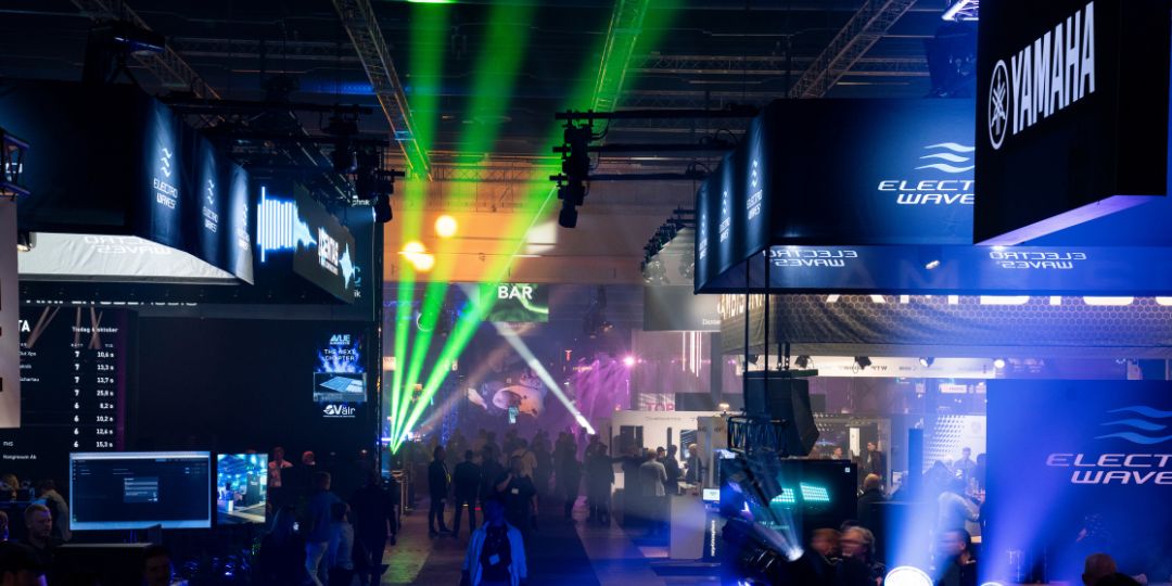 Namnlös design (5) Interaktiv ljusinstallation på mässa: genomskinlig, neonbelyst polyeder med besökare inuti och staplade LED-kuber intill.